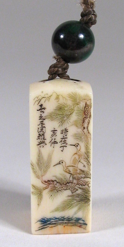 DESCRIPTION: A small, etched ivory seal with an engraved scene of birds in a pine tree.  At the top center is a three-line Chinese inscription in tiny characters.  The top is pierced with two holes through which a silk cord is threaded and secured by a green jade bead.  The seal itself leaves a positive (or red) impression when inked. Dating from the 19th C. Qing Dynasty, this seal is in excellent condition. DIMENSIONS: 1 1/8” high (2.8 cm) not including bead. <div id='rater_target1170582'></div>
