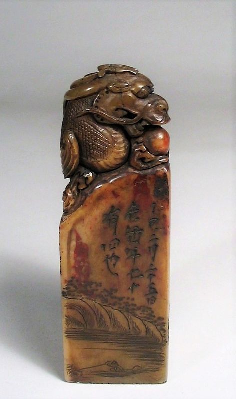 SOLD<br /><br />
DESCRIPTION:  A large and masterfully carved Chinese shou shan stone (soapstone) seal in tall rectangular form, the knob carved with a crouching dragon having both wings tucked back covering its sides, and whose mouth is poised to grasp the sacred pearl. On each flat surface of the base are engraved inscriptions and characters among idyllic scenes of rivers with boats, hills, houses and pavilions.  The bottom seal characters leave a positive (red) impression.  An outstanding seal in very good condition.  DIMENSIONS:  4 3/8” high (11.1 cm) x 1.5” square (3.8 cm).  
<div id='rater_target1366579'></div>
